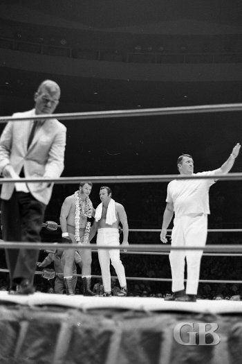 A lei draped Don Leo Jonathan chats with Nick Bockwinkel as announcer Jim Lathrop leaves the ring before the start of the match