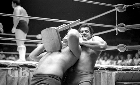 Pedro Morales chokes Nick Bockwinkel with a stool while outside the ring.